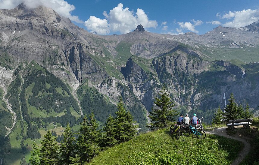 <p>Drei Mountainbiker sitzen auf einer Bank und geniessen das saftig grüne Bergpanorama auf die Engstligenfälle.</p>